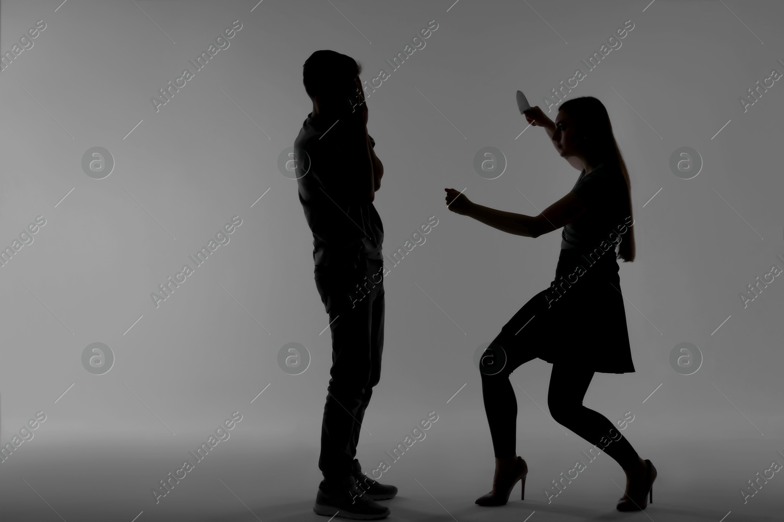 Photo of Domestic violence. Silhouette of woman with knife threatening her husband on grey background