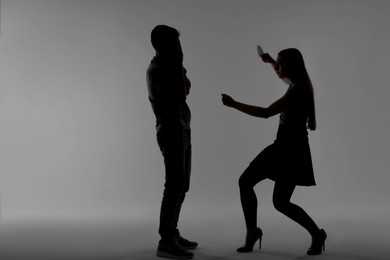 Photo of Domestic violence. Silhouette of woman with knife threatening her husband on grey background