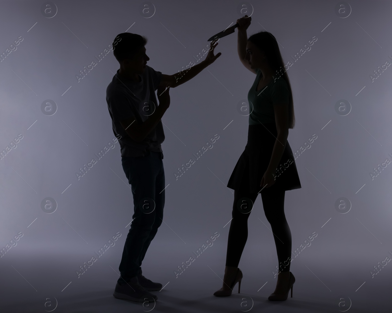 Photo of Domestic violence. Silhouette of woman with knife threatening her husband on grey background