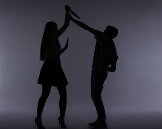 Domestic violence. Silhouette of woman with knife trying to kill her husband on grey background