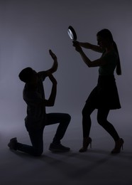 Photo of Domestic violence. Silhouette of woman with frying pan threatening her husband on grey background