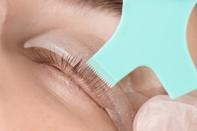 Photo of Eyelash lamination procedure. Esthetician applying adhesive on woman's lashes, closeup