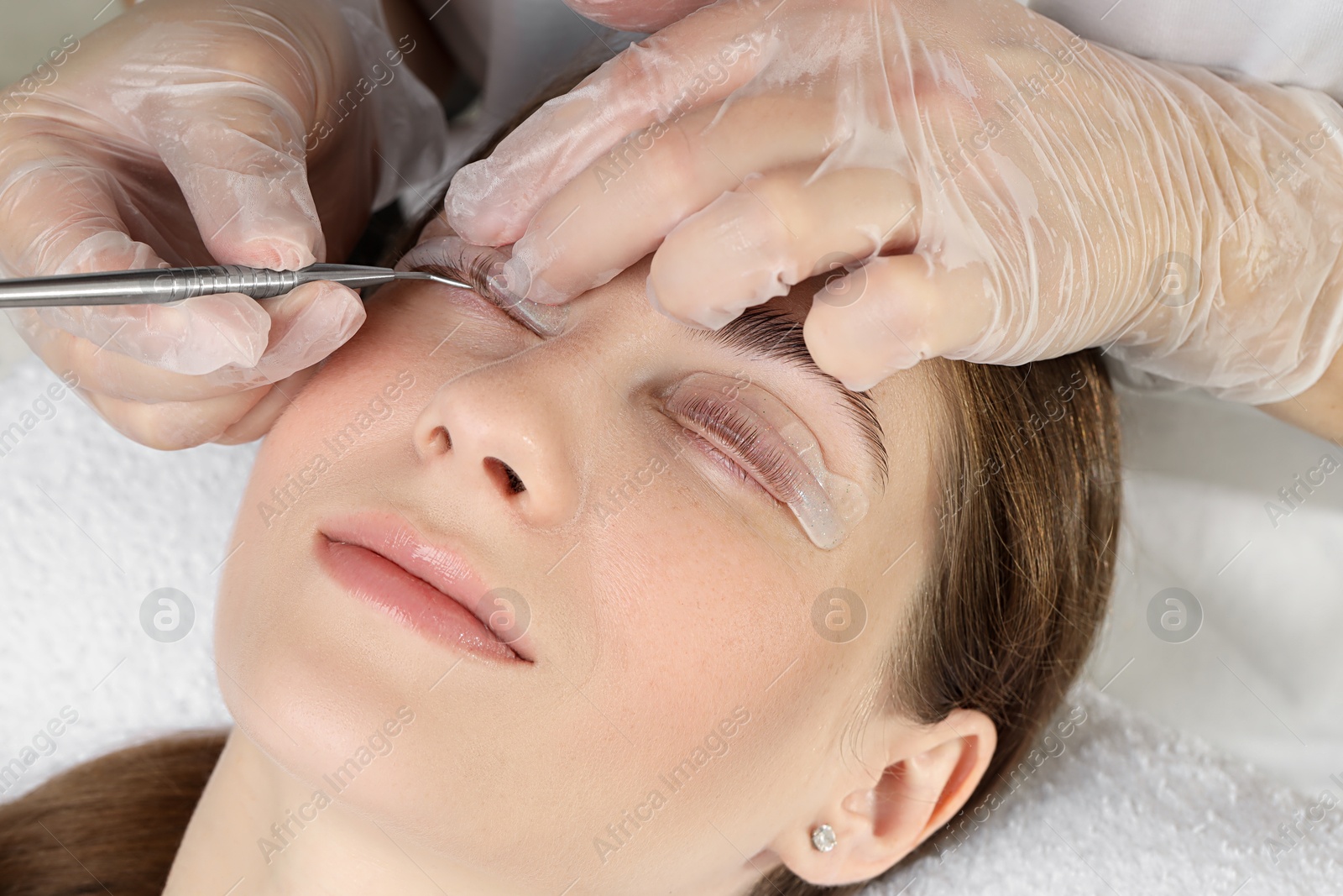 Photo of Eyelash lamination procedure. Esthetician untangling woman's lashes in beauty salon, closeup