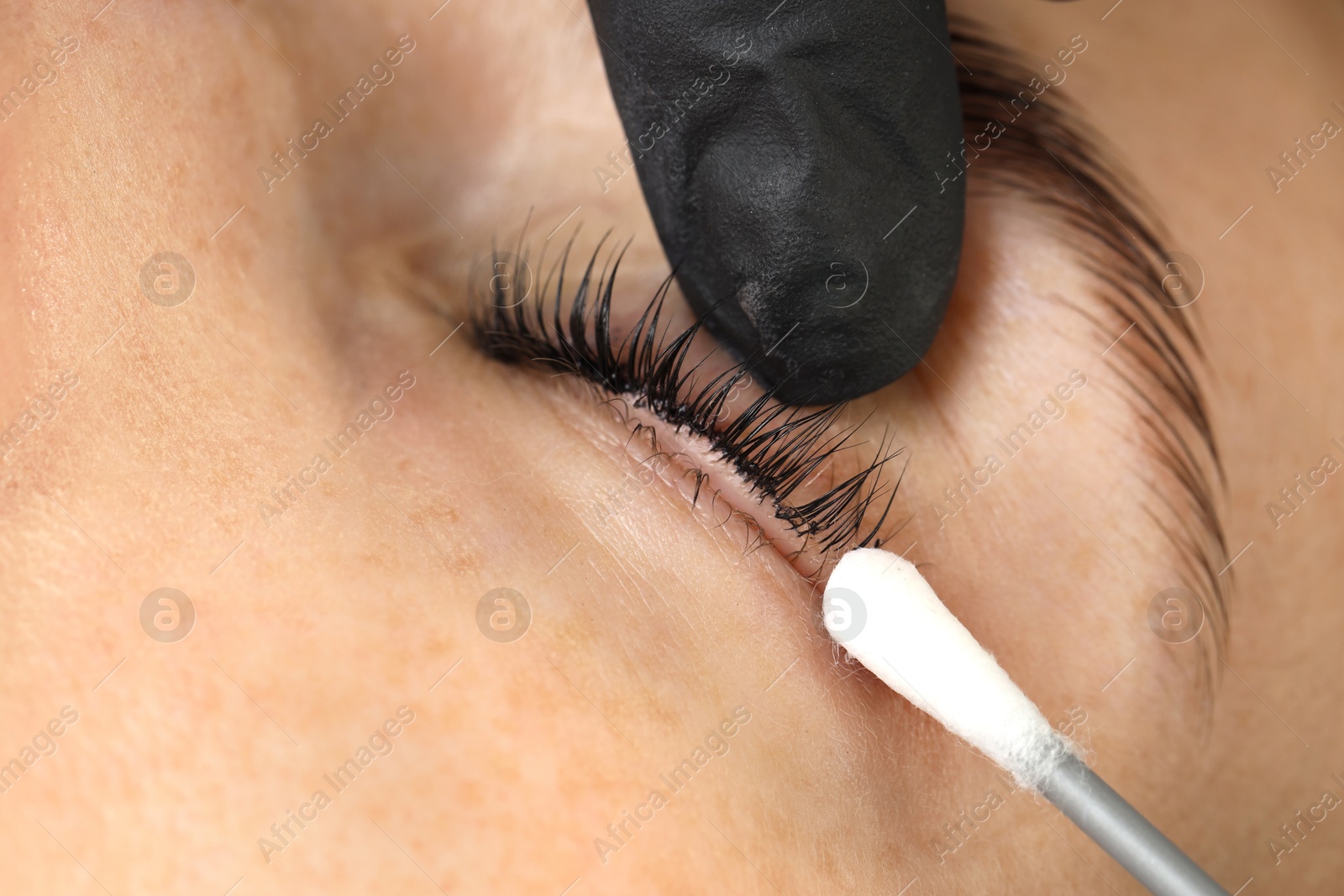 Photo of Esthetician cleaning woman's lashes after lamination procedure, closeup