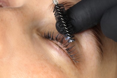 Photo of Esthetician brushing woman's lashes after lamination procedure, closeup