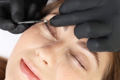 Photo of Esthetician brushing woman's lashes after lamination procedure, closeup