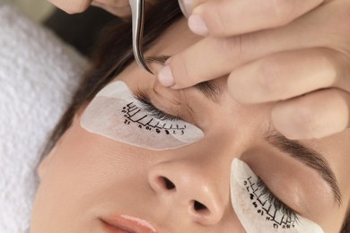 Photo of Esthetician taping woman's eyelid before lash extensions procedure in beauty salon, closeup