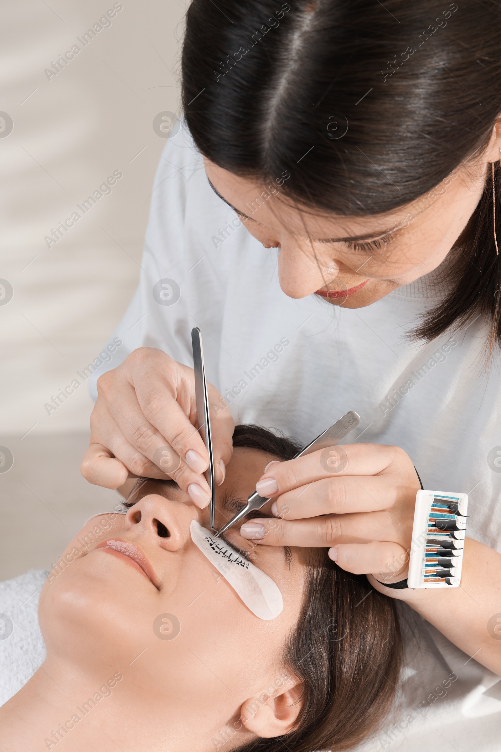 Photo of Esthetician applying lash extensions on natural ones in beauty salon, closeup