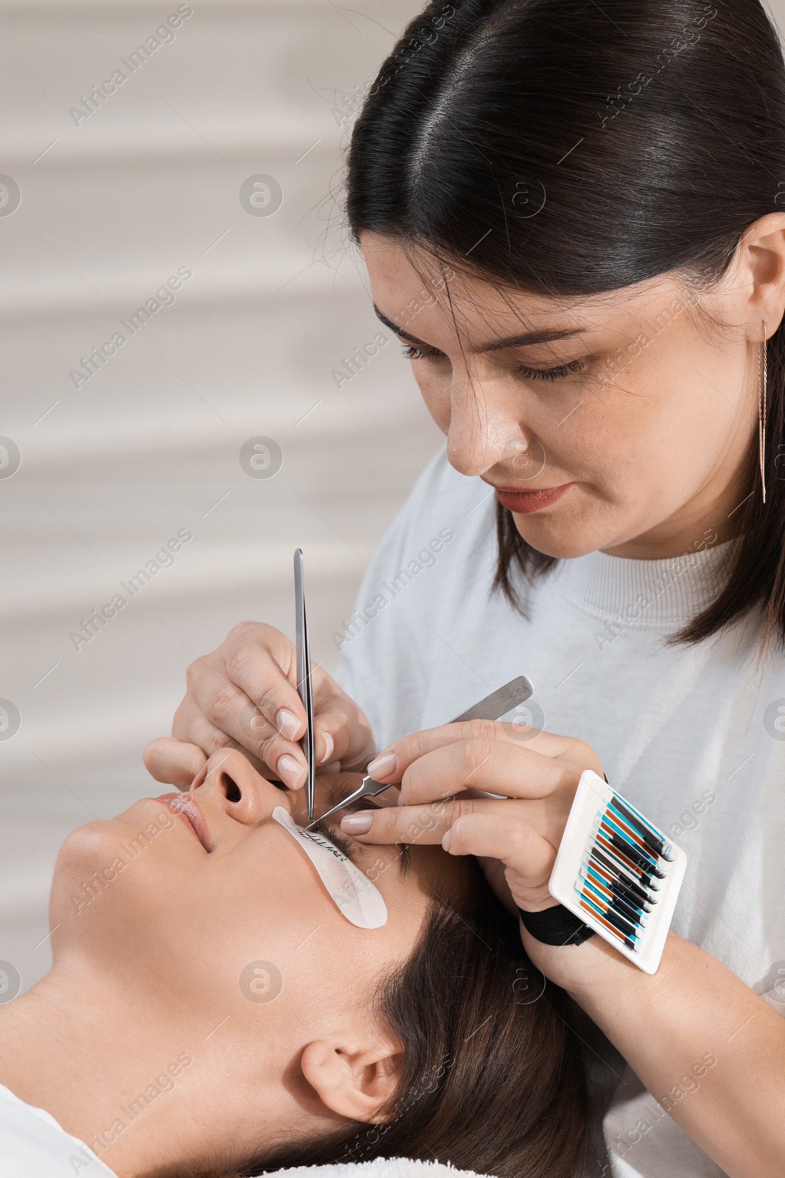 Photo of Esthetician applying lash extensions on natural ones in beauty salon, closeup