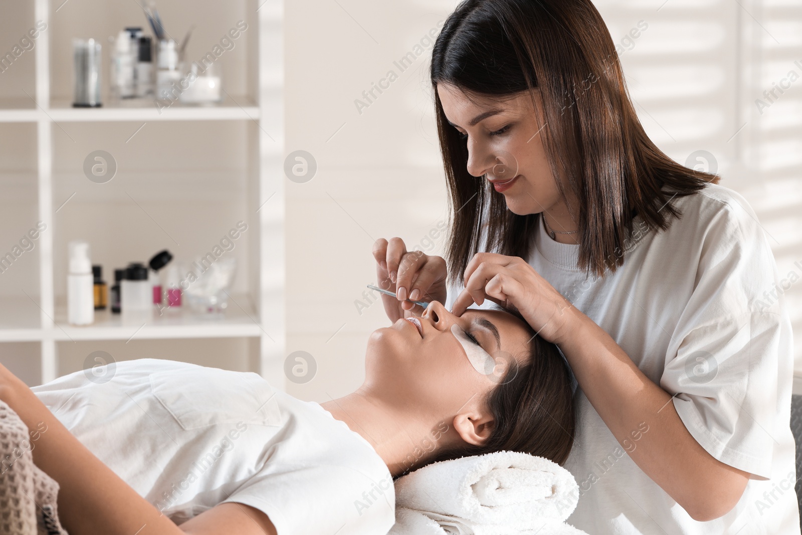 Photo of Esthetician brushing woman's lash extensions during procedure in beauty salon