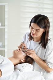 Photo of Esthetician applying lash extensions on natural ones in beauty salon