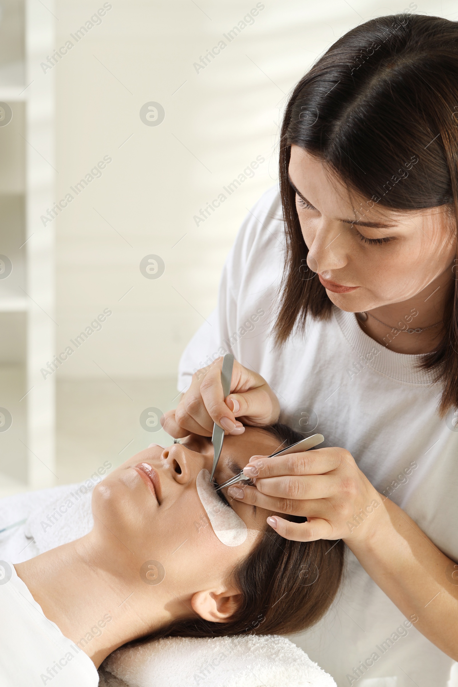 Photo of Esthetician applying lash extensions on natural ones in beauty salon