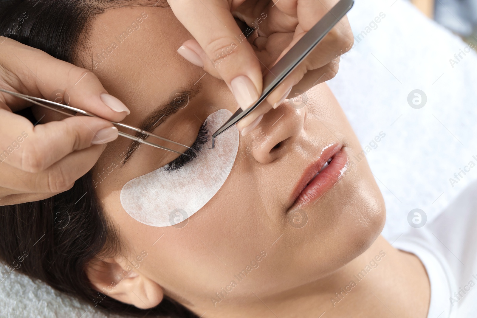 Photo of Woman undergoing lash extensions procedure in beauty salon, closeup