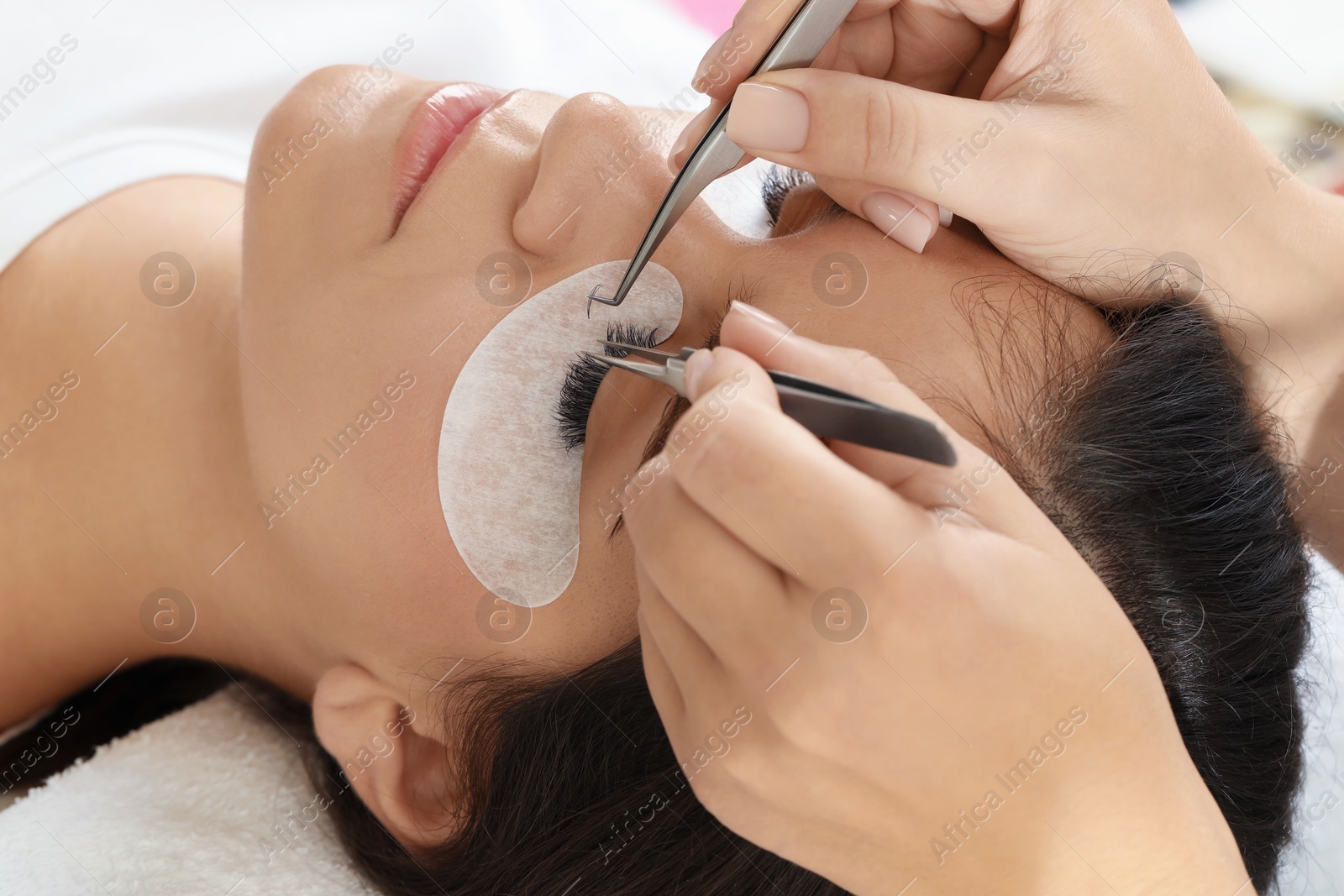 Photo of Woman undergoing lash extensions procedure in beauty salon, closeup