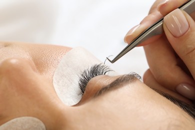 Photo of Woman undergoing lash extensions procedure in beauty salon, closeup