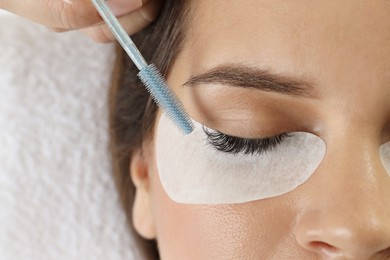 Photo of Esthetician brushing woman's lash extensions during procedure in beauty salon, closeup