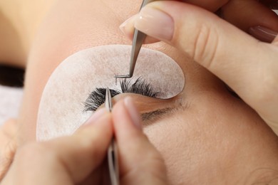 Photo of Woman undergoing lash extensions procedure in beauty salon, closeup