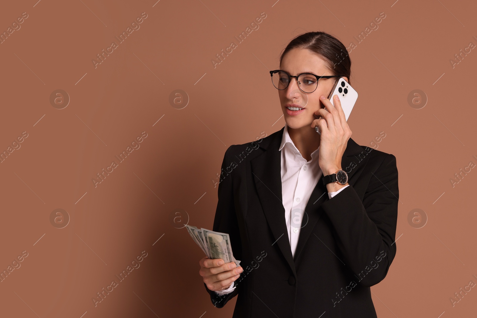 Photo of Banker with dollar banknotes talking on smartphone against brown background, space for text