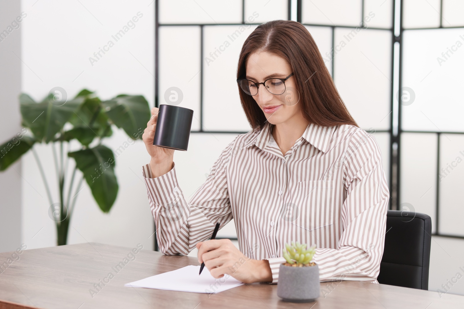 Photo of Banker holding cup of drink working with document at wooden table in office