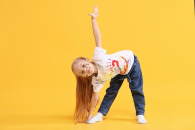 Photo of Cute girl smeared in paint on orange background. Space for text