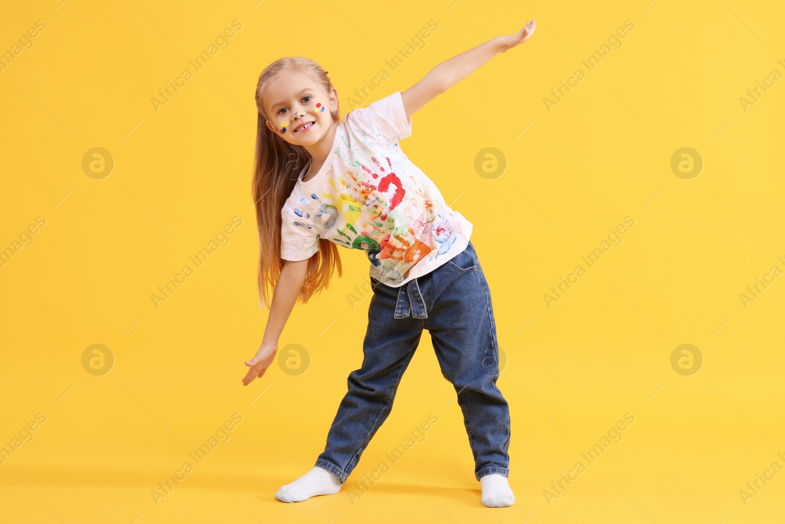 Photo of Smiling girl smeared in paint on orange background