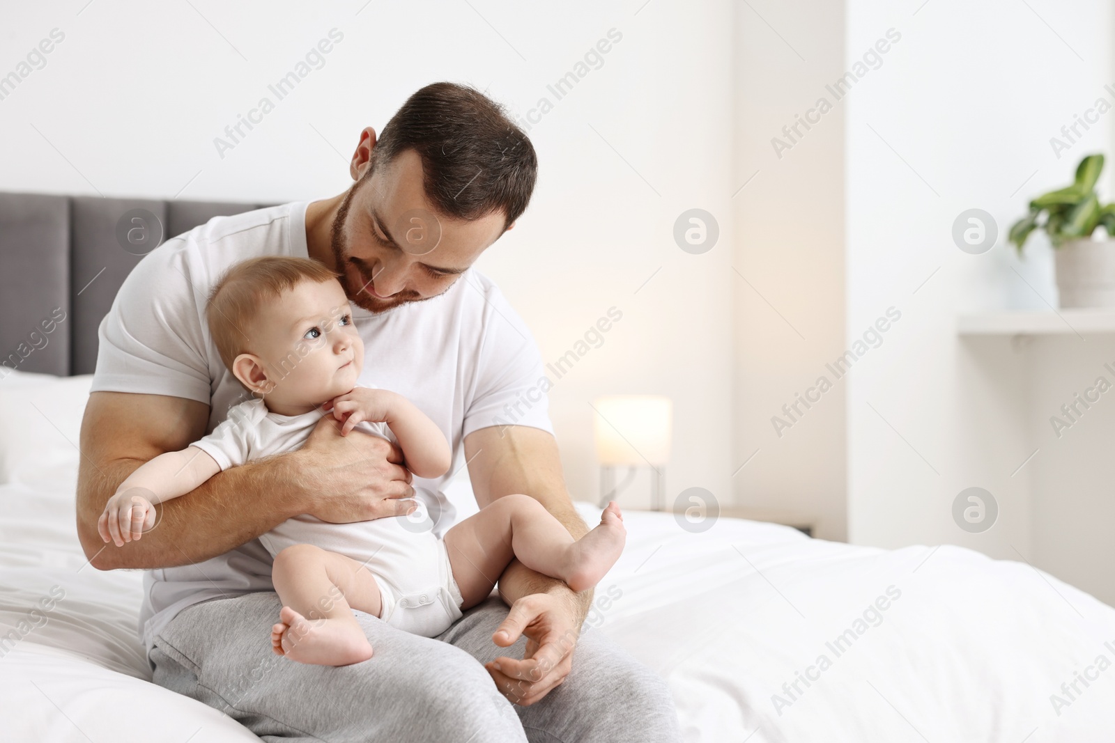 Photo of Father with his little baby on bed at home. Space for text