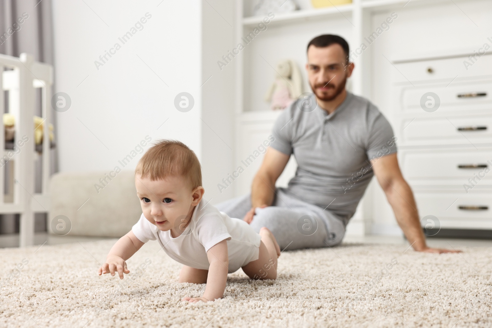 Photo of Father watching his little baby learning to crawl at home, selective focus