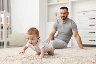 Photo of Father watching his little baby learning to crawl at home, selective focus