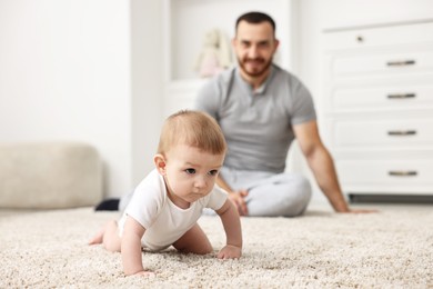 Photo of Father watching his little baby learning to crawl at home, selective focus