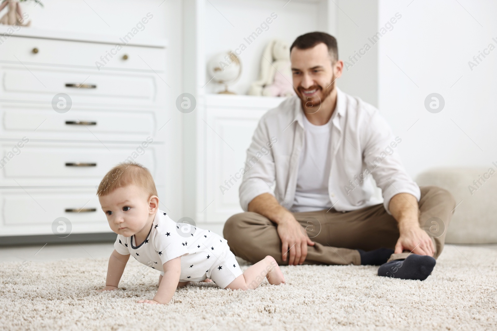 Photo of Father watching his little baby learning to crawl at home, selective focus