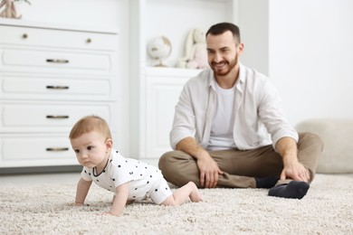 Photo of Father watching his little baby learning to crawl at home, selective focus