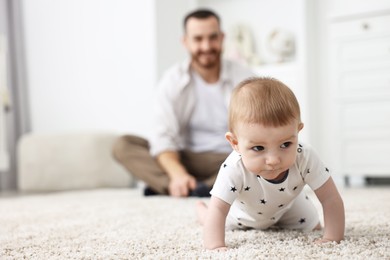 Photo of Father watching his little baby learning to crawl at home, selective focus. Space for text