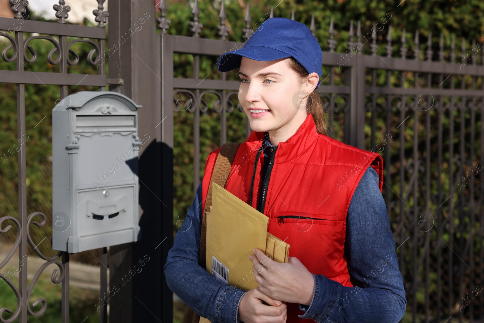 Photo of Mailwoman in uniform with envelopes outdoors. Postal service