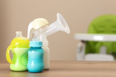 Photo of Feeding bottles with milk and breast pump on wooden table indoors, space for text