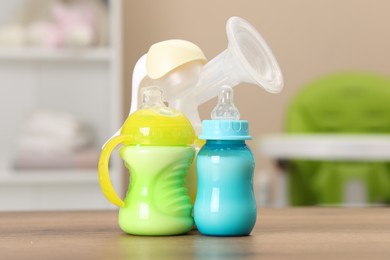 Feeding bottles with milk and breast pump on wooden table indoors