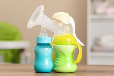 Feeding bottles with milk and breast pump on wooden table indoors