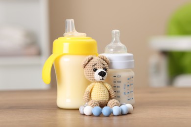 Photo of Feeding bottles with milk and toys on wooden table indoors