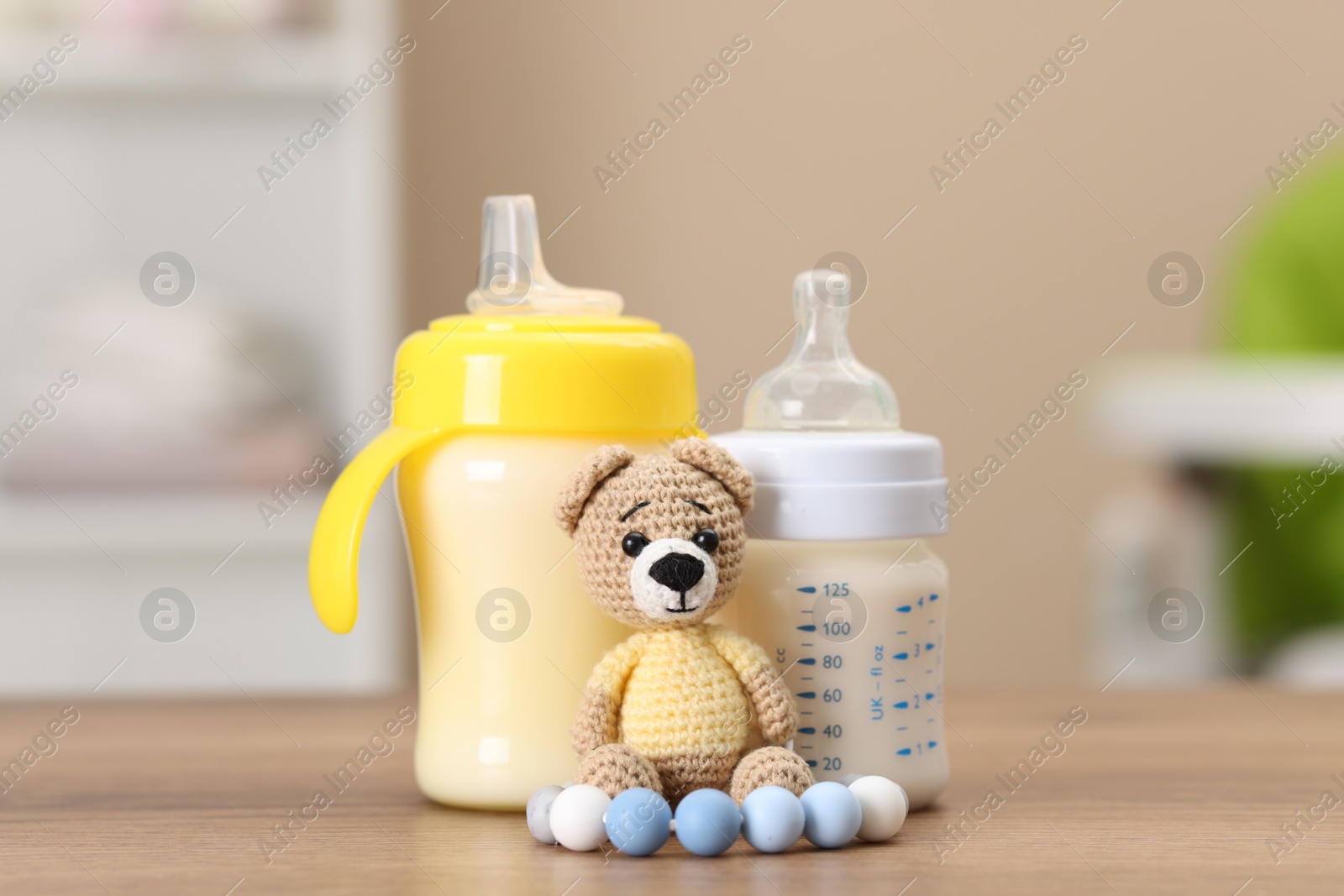 Photo of Feeding bottles with milk and toys on wooden table indoors