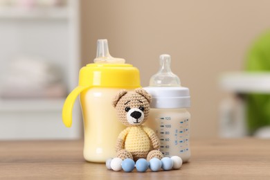 Photo of Feeding bottles with milk and toys on wooden table indoors