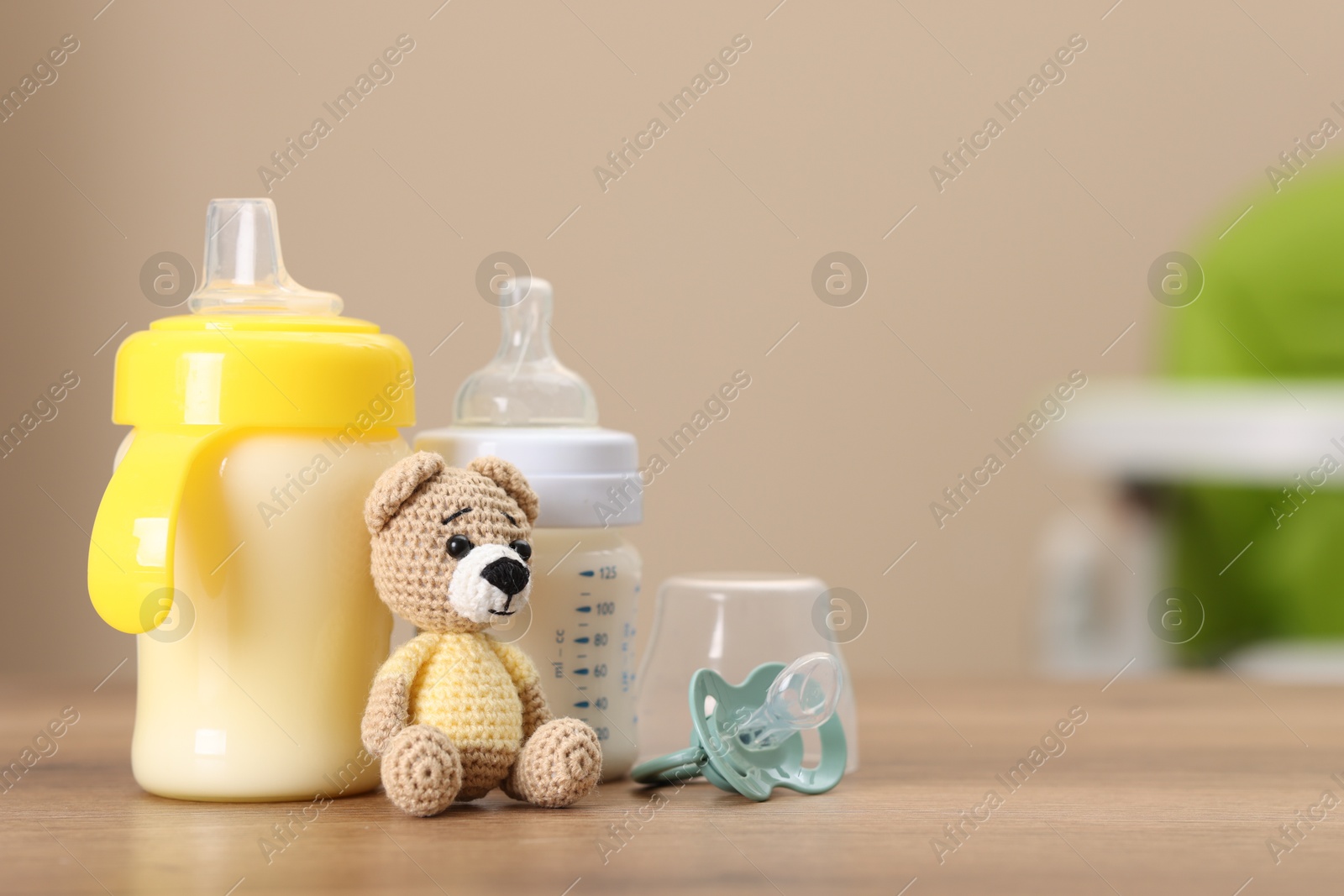 Photo of Feeding bottles with milk, toy and pacifier on wooden table indoors, space for text