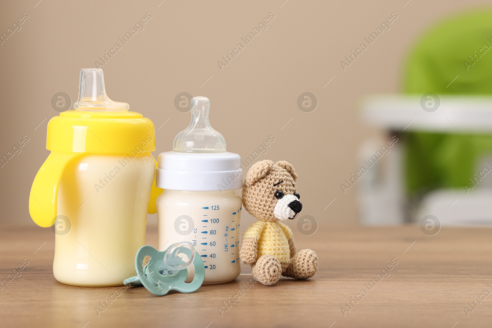 Photo of Feeding bottles with milk, toy and pacifier on wooden table indoors, space for text