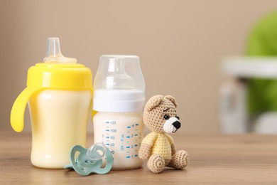 Photo of Feeding bottles with milk, toy and pacifier on wooden table indoors, space for text