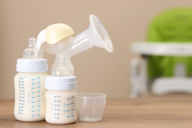 Photo of Feeding bottles with milk and breast pump on wooden table indoors, space for text