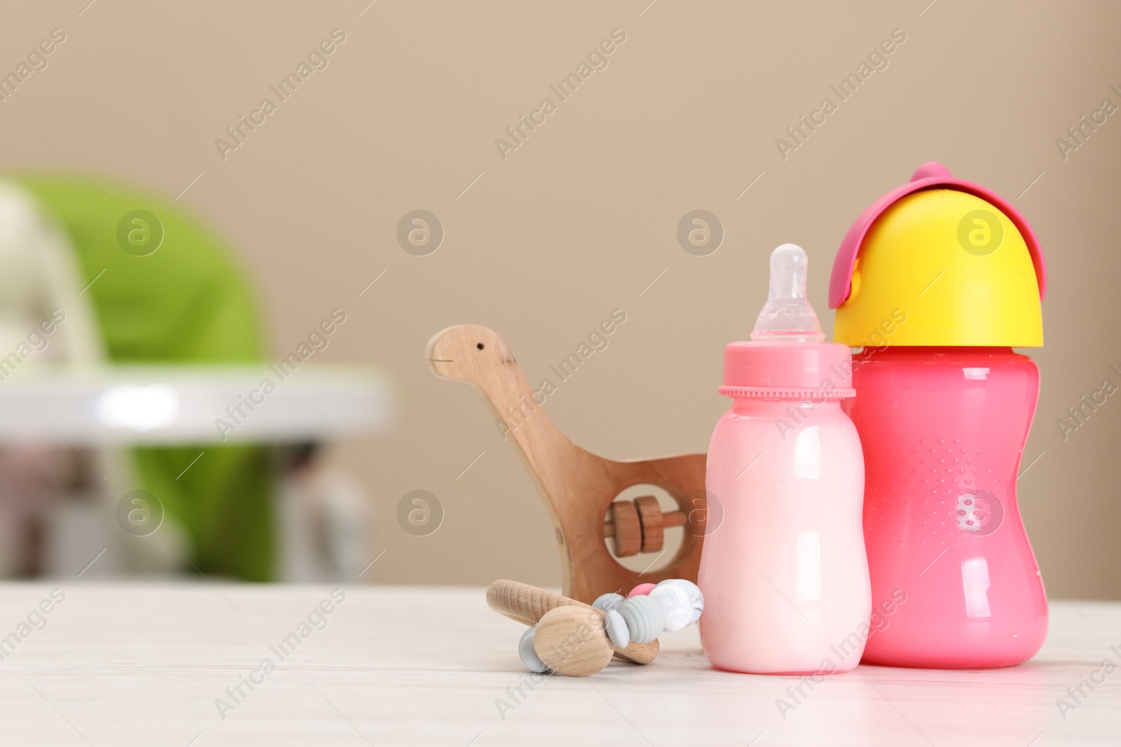 Photo of Feeding bottles with milk and toys on white wooden table indoors, space for text