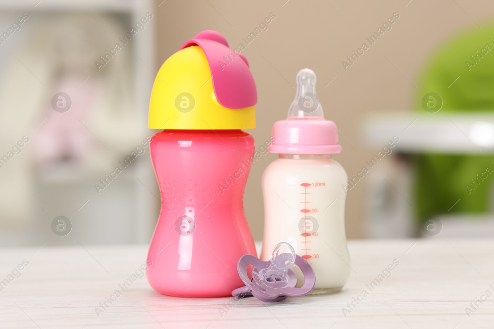 Photo of Feeding bottles with milk and pacifier on white wooden table indoors