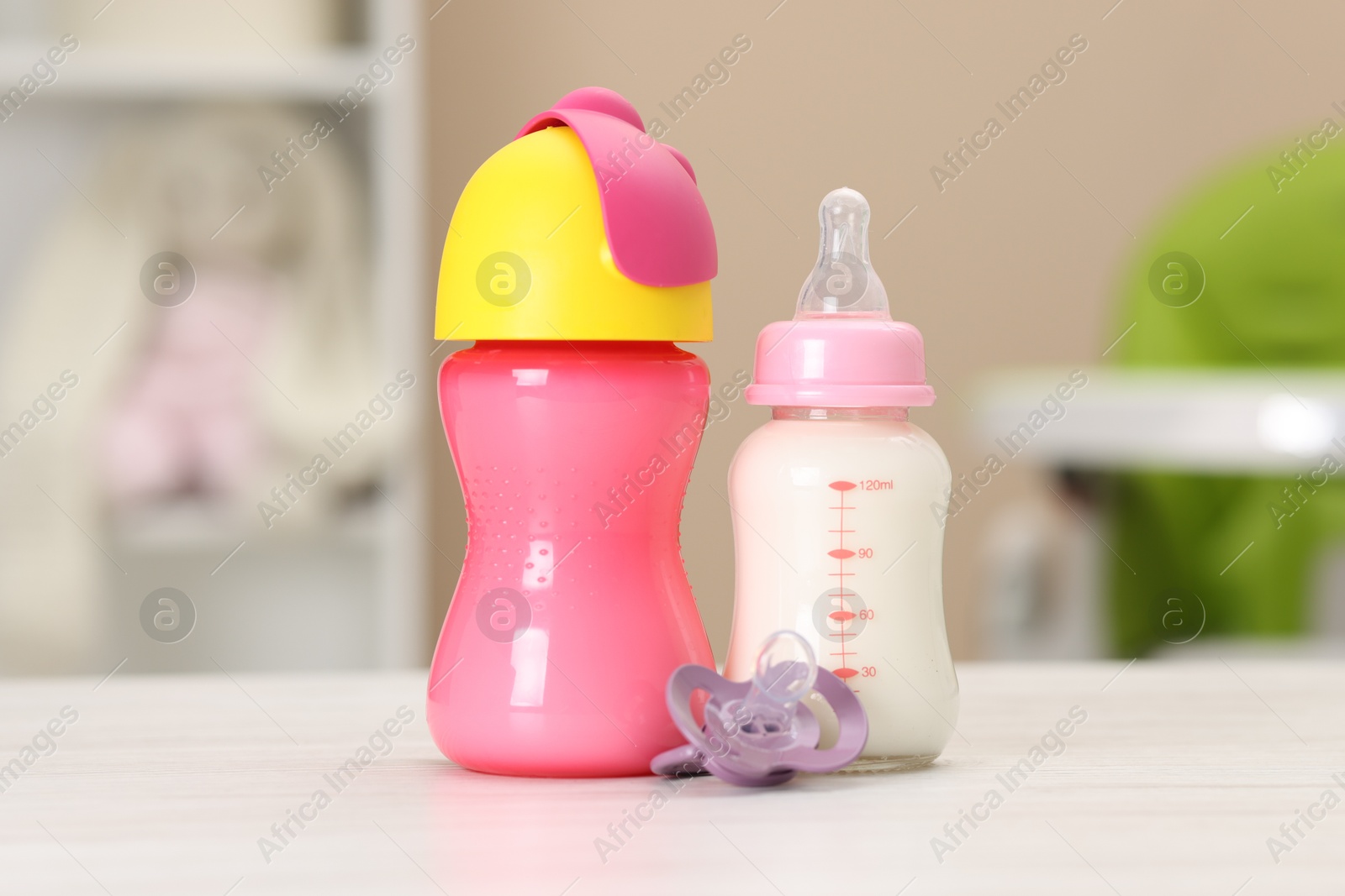 Photo of Feeding bottles with milk and pacifier on white wooden table indoors