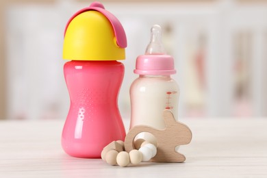 Photo of Feeding bottles with milk and toy on white wooden table indoors