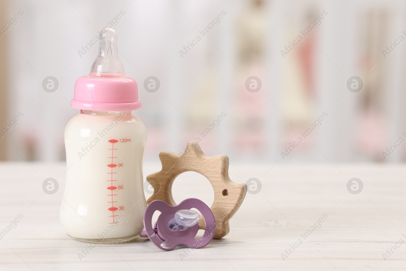 Photo of Feeding bottle with milk, pacifier and toy on white wooden table indoors