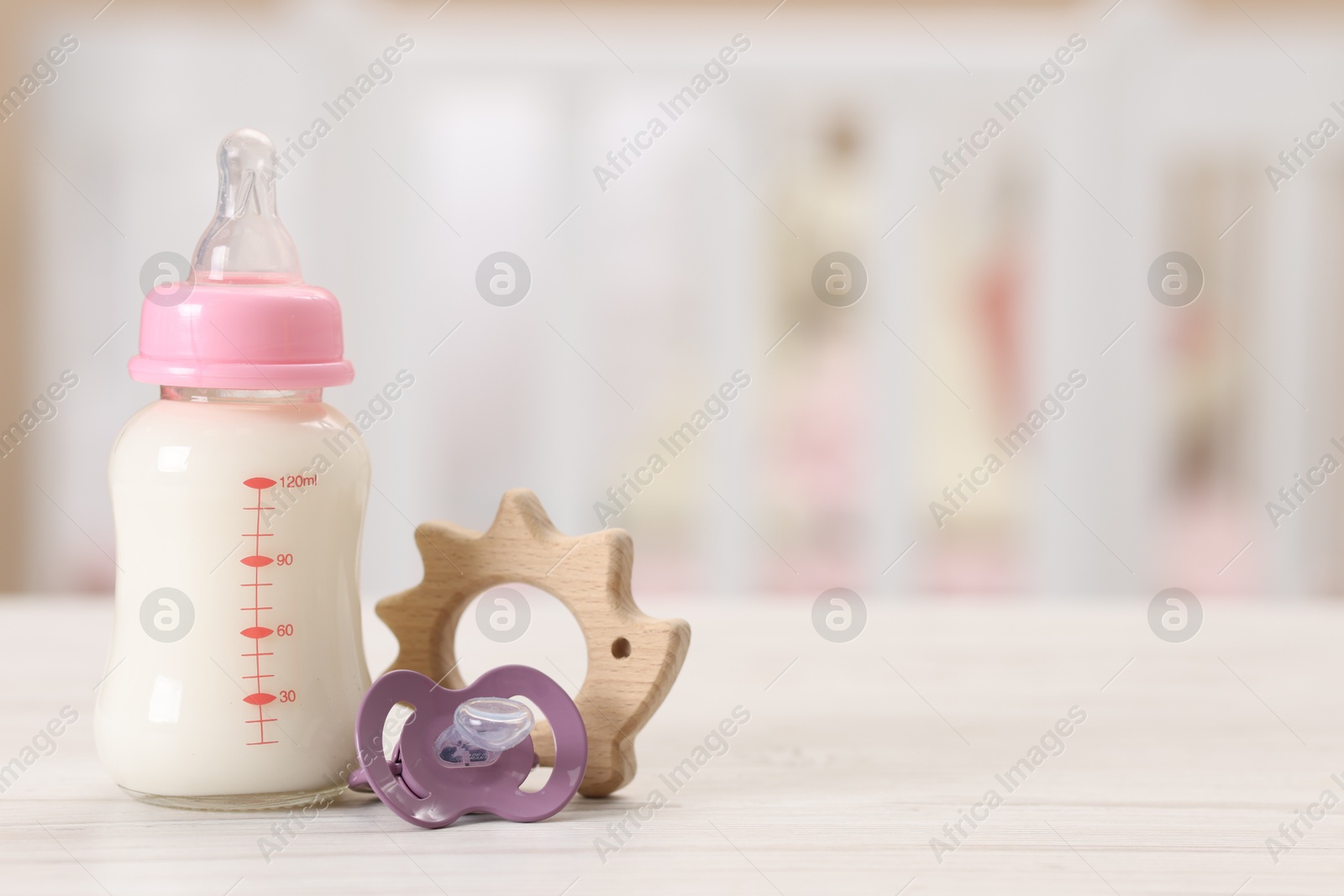 Photo of Feeding bottle with milk, pacifier and toy on white wooden table indoors