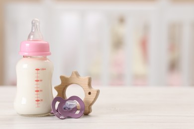 Photo of Feeding bottle with milk, pacifier and toy on white wooden table indoors